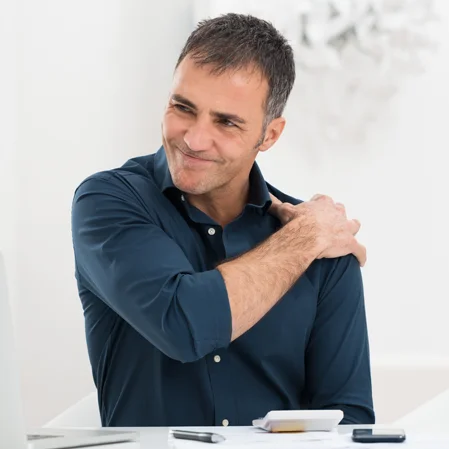 A man working in an office gripping his shoulder in pain